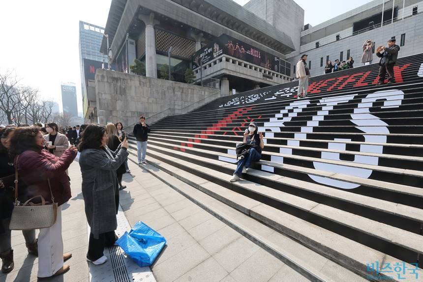 방탄소년단(BTS)의 서울 광화문광장 컴백 공연을 앞둔 지난 3월 17일 서울 종로구 세종문화회관 계단에서 외국인 관광객이 BTS 컴백 공연 관련 래핑 광고를 배경으로 기념촬영을 하고 있다. 사진=임준선 기자